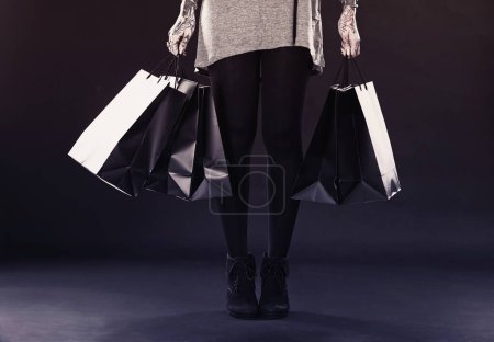 Woman, legs and shopping bags for fashion in studio on dark background with retail, discount and clothes. Female person, tattoo and edgy style with creative look, body ink and art for self care.