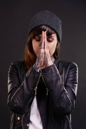 Photo for Praying, tattoo or woman in studio for fashion in leather jacket on black background for edgy style. Forgive, hope or cool female punk model with ink for unique art, aesthetic or creative expression. - Royalty Free Image