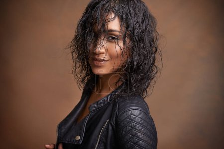 Photo for Fashion, portrait and leather jacket with woman, aesthetic and stylish clothes on brown studio background. Face, Indian person and model with mockup space and happy girl with bold and cool makeup. - Royalty Free Image
