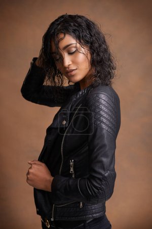 Photo for Thinking, beauty and woman with fashion, leather jacket and confident girl on a brown studio background. Stylish clothes, model and Indian person with casual outfit and happy with edgy and trendy. - Royalty Free Image