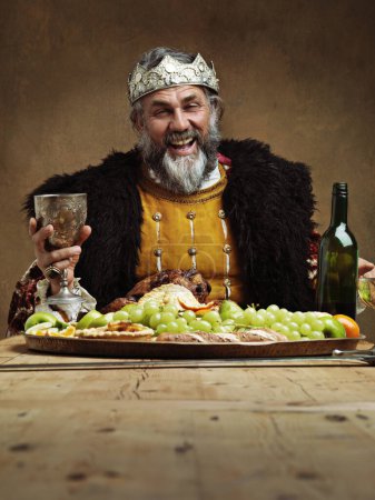 Téléchargez les photos : Roi, festin et heureux dans la table avec verre de vin comme seigneur sur la salle à manger pour la tradition, la culture et le repas dans le palais. Portrait, monarque et chef avec buffet ou souper à la fête royale avec couronne. - en image libre de droit