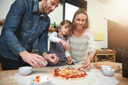 Photo for Learning, smile and family baking pizza in kitchen together, bonding and happy in home. Food, mother and father with kid cooking, teaching and help parents prepare for lunch with cheese at table. - Royalty Free Image