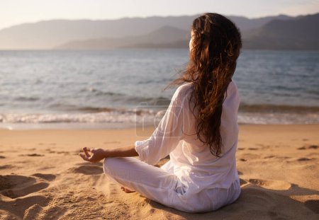 Foto de Vista trasera, mujer y meditación en la playa con pose de loto, mindfulness y zen con aire fresco para una calma al aire libre. Océano, brisa y viaje con yoga para la salud, la paz mental y la curación holística. - Imagen libre de derechos