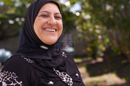 Foto de Mujer musulmana, retrato y feliz en la naturaleza en hijab, relajarse y persona madura de vacaciones en el aire libre. Mujer islámica, sonrisa cara y religión en la bufanda en el jardín y sol en la mañana en la jubilación. - Imagen libre de derechos