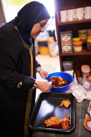 Photo for Muslim woman, cooking or food in kitchen for family dinner or malay spice for arabic cuisine. Islam mother or meal preparation of chicken for grill, hijab or islamic tradition or female role in home. - Royalty Free Image