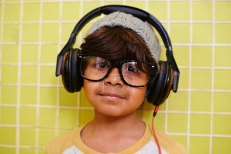 Foto de Niño, retrato y gafas con auriculares en casa con música y streaming. Radio, gafas y moda juvenil con un chico indio hipster escuchando audio con estilo cool en una casa con marcos. - Imagen libre de derechos