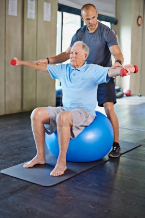 Fisioterapeuta, auxiliar y hombre mayor con pesas, entrenamiento y apoyo de ancianos para el cuidado. Hombres, gimnasio y ejercicio para la salud, bienestar y coaching con bola de yoga para rehabilitación y bienestar maduros.