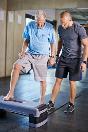 Photo for Physiotherapist, helping and senior man with cardio, training and elderly support for care. Men, gym and exercise for health, wellness and coaching with aerobic step for mature rehab and wellbeing. - Royalty Free Image