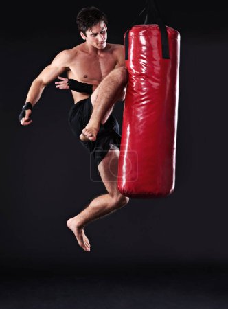 Téléchargez les photos : Arts martiaux, homme et entraînement avec genou dans un sac de boxe pour le développement des compétences en studio sombre avec puissance. Homme, figure et fond noir dans la salle de gym pour la forme physique, muay thai saut et la force. - en image libre de droit