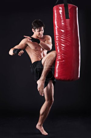 Photo for Man, fighter and boxing bag with kick in studio for self defence workout, martial arts or black background. Male person, wellness and mockup space for strength training with gym, fitness or sport. - Royalty Free Image