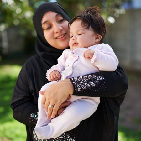 Foto de Musulmanes, mujeres y bebés se abrazan al aire libre, felices en el jardín con la madre y el niño para la celebración del Eid. Maternidad, familia y fiesta islámica con hiyab, bebé y abrazo con sonrisa en el patio trasero para la vinculación. - Imagen libre de derechos