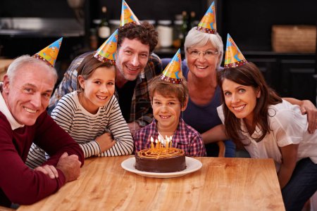 Téléchargez les photos : Famille, anniversaire et portrait avec garçon, parents et grands-parents avec gâteau et bougies. Joyeux, sourire et dessert avec les enfants et célébration avec la nourriture de l'événement et chapeaux de fête à une table. - en image libre de droit