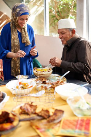 Téléchargez les photos : Aïd, vacances et famille avec de la nourriture pour la célébration musulmane avec l'homme donnant à la femme une assiette à table. Accueil, buffet ou faim de plat de dessert ou excité pour la viande en vacances de festival pour la religion Islam. - en image libre de droit
