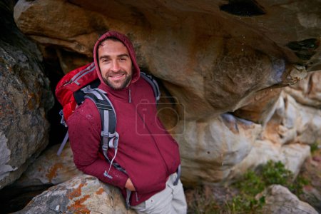 Photo for Man, portrait and hiking by mountains in nature with backpack, gear and rocks for fitness, health and exercise. Male explorer, smile and trekking outdoor with plants, bag and boulders for adventure. - Royalty Free Image