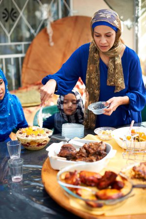 Foto de Eid, día de fiesta y familia con comida para la celebración musulmana con la madre dando a su hijo un plato en la mesa. Hogar, buffet y mamá sirven plato de postre o carne con amor y cuidado en vacaciones por la religión. - Imagen libre de derechos