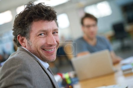 Photo for Happy, portrait and creative man coworking in office with team and planning project with laptop on desk. Mature, employee and productivity in collaboration, cooperation or development of ideas. - Royalty Free Image