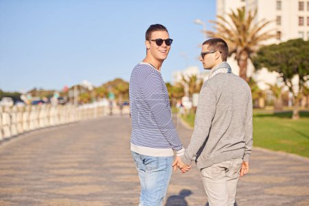 Photo for Gay couple, smile and walk outdoor for trip and travel on vacation for rest and break in summer. Young men, happiness and together in nature for relationship and recreation for joy and love. - Royalty Free Image