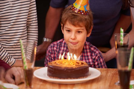 Téléchargez les photos : Excité, enfant et bougies sur le gâteau d'anniversaire à la fête et faim de nourriture sur la table. Heureux, enfant et famille ensemble à l'événement pour se détendre et profiter du développement de la croissance du garçon à la maison. - en image libre de droit