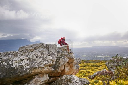Photo for Man, cliff and relax on outdoor hike in nature, mountain and peace or calm on rocks for wellness. Male person, exercise and travel with backpack on vacation, adventure and explore bush for fitness. - Royalty Free Image