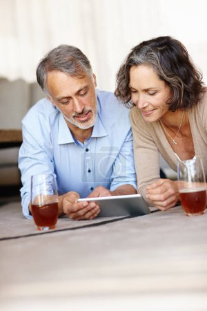 Photo for Old couple on the floor, home and love with tablet, relaxing and bonding together with internet, relationship and social media. Apartment, senior woman and mature man on the ground, tech and marriage. - Royalty Free Image
