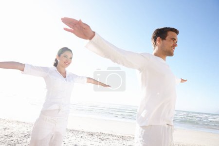 Foto de Equilibrio, yoga y pareja en la playa para fitness, calma y bienestar con sol, viajes y mindfulness juntos. Calma, paz y luz natural con aire fresco, gente feliz y equilibrio energético para aura. - Imagen libre de derechos