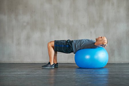 Photo for Man, fitness and stretching with exercise ball for workout, training or balance at gym. Active male person lying on round object, equipment or support for warm up, health and wellness on mockup space. - Royalty Free Image