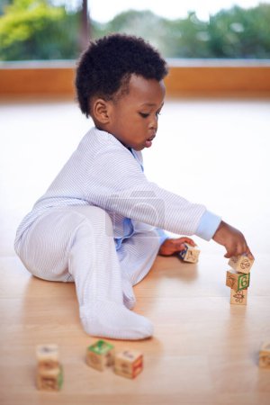 Foto de Bebé negro, jugando y bloques de madera en casa en el suelo para el desarrollo infantil, el crecimiento y las habilidades motoras. Niño africano, tiempo de juego y la construcción de la pieza en casa en la sala de estar para la diversión, la infancia y el aprendizaje. - Imagen libre de derechos