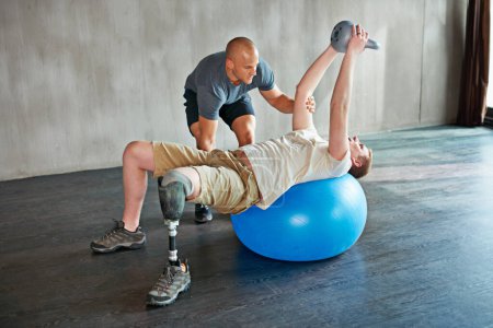 Photo for Patient with disability, physiotherapist and help with kettlebell for exercise at gym for recovery, strength and healthcare rehabilitation. Physiotherapy, amputee or man for consultation with ball. - Royalty Free Image