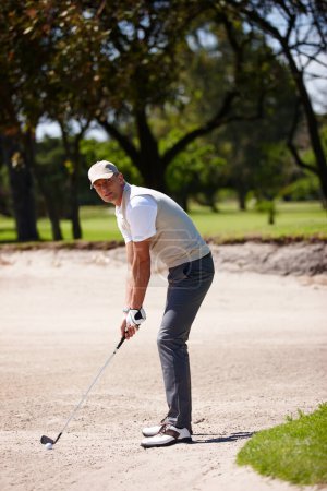 Photo for Man, portrait and golfer with club for stroke, point or strike in sand pit by grass field in nature. Male person or sports player getting ready to swing ball in dirt for game or match on golf course. - Royalty Free Image