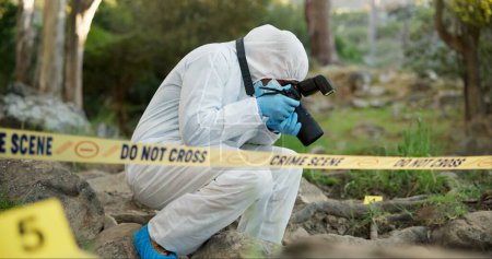 Photo for Forensic, photographer and police tape at crime scene for investigation in forest with evidence and safety hazmat..Csi quarantine, expert investigator and pictures for observation and case research. - Royalty Free Image