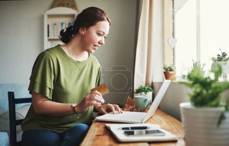 Foto de Tengo que comprar esto. Recorte de una atractiva joven empresaria sentada sola en su oficina en casa y usando su computadora portátil para ir de compras en línea - Imagen libre de derechos