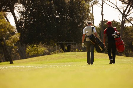 Téléchargez les photos : Randonnée pédestre, amis et hommes ensemble sur le terrain de golf avec sac de golf pour la formation, la santé et le travail d'équipe. Hommes, équipement sportif et exercice pour l'activité avec vêtements de sport, pelouse et arbres en plein air. - en image libre de droit