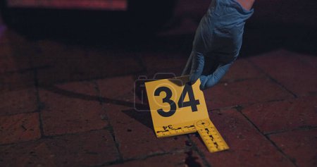 Photo for Evidence marker, hand of csi and crime scene with forensic on floor at night for investigation of murder. Professional, expert in gloves and case investigator with observation and search with blood. - Royalty Free Image