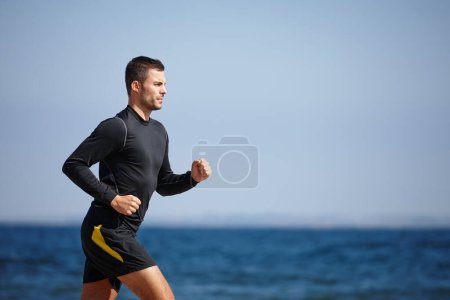 Photo for Man, running and blue sky by ocean for cardio with fitness goals, exercise and health workout. Male person, training and nature at beach with sports athlete for wellness, strong body and endurance. - Royalty Free Image
