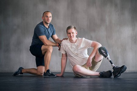 Trainer, person with a disability and prosthetic leg and posing in physiotherapy, studio and gym ball. Male people, physiotherapist and amputee for wellness, fitness and exercise in sports center.