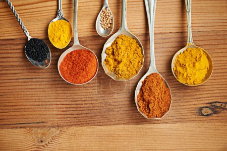 Photo for Spoons, spice and selection of powder for seasoning on kitchen table, turmeric and paprika for meal. Top view, condiments and options for spicy cooking in Indian culture, cumin and food preparation. - Royalty Free Image