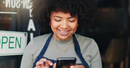 Foto de Mujer negra, teléfono y cafetería abierta por puerta para comunicación, redes sociales o networking. Mujer africana feliz persona o camarera sonrisa en el teléfono inteligente móvil en el chat en línea o mensajes de texto en la cafetería. - Imagen libre de derechos