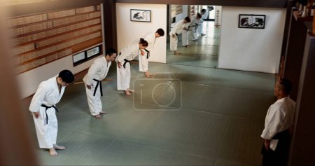 Photo for Japanese people, bow and learning aikido in dojo place in training and modern martial arts class of self defence. Group, black belt students and sensei with instruction and respect for discipline. - Royalty Free Image