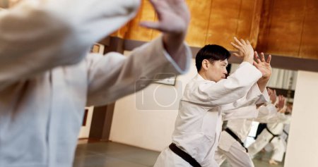 Photo for Aikido class, group and people for martial arts, strike or together for combat at training, gym or dojo. Black belt students, fight and exercise for workout, fitness and conflict at Japanese club. - Royalty Free Image