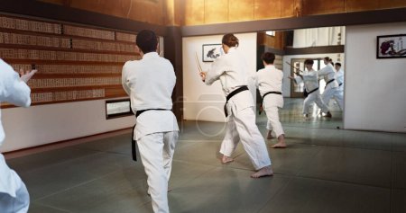 Photo for Aikido group, fight and bokken of martial arts, weapon or black back students at training, gym or dojo. Japanese people, wood sword and club for exercise, workout or fitness in conflict with battle. - Royalty Free Image