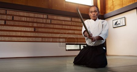 Foto de Aikido con sensei en el suelo, espada de madera y entrenamiento para fitness, lucha o acción en el gimnasio tradicional en Japón. Ejercicio, práctica y hombre maduro en dojo con cinturón negro en las artes marciales japonesas - Imagen libre de derechos