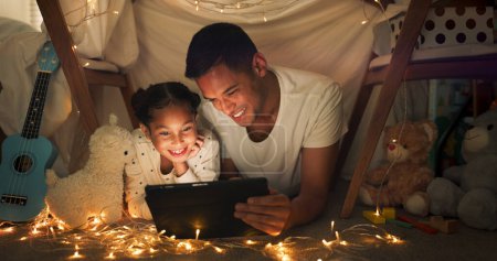 Foto de Tienda de campaña, padre y chica en la tableta por la noche viendo películas, juegos en línea y cuentos para dormir con luces de hadas. Familia feliz, sonrisa y papá con el niño en el dormitorio en la tecnología digital para la vinculación, relajarse y amar. - Imagen libre de derechos