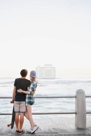 Photo for Couple, rear view and hug on beach for travel with mockup space, adventure and promenade date. Gen z skater, people and skateboard on boardwalk for bonding, embrace and outdoor fun with morning waves. - Royalty Free Image
