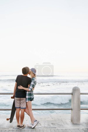 Photo for Couple, kiss and romance on beach for date with mockup space, adventure and skateboard on promenade. Skater, people and hugging on boardwalk for bonding, embrace and outdoor travel with sea waves. - Royalty Free Image