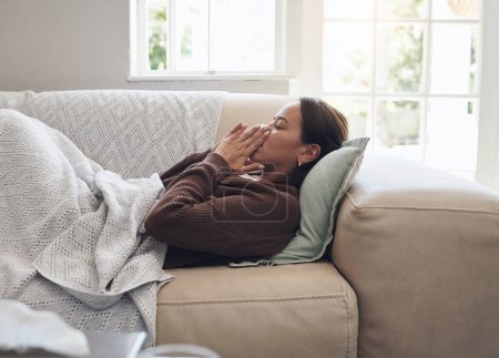 Photo for Sick woman, sneeze and blowing nose with illness, flu or cold on living room sofa at home. Young female person with tissue for bacteria, fever or influenza in fatigue or rest on lounge couch at house. - Royalty Free Image