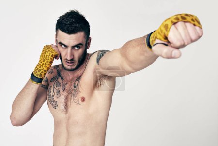 Photo for Man, fight swing and punch for martial arts, self defense and exercise for physical strength and training in studio. Angry male fighter, glove bandage and tattoo for combat and recreation sport. - Royalty Free Image