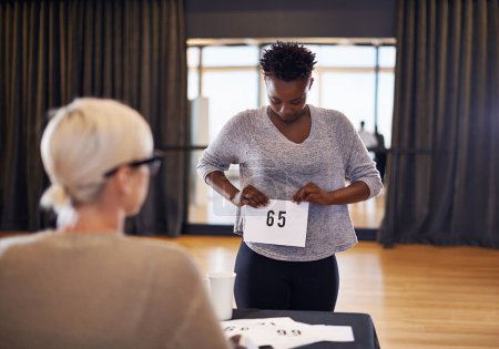 Number, judge and woman in casting audition to sign up for performance or acting on a stage in theater. Happy actress, competition or dancer ready for dancing at academy in talent show in auditorium.