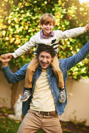 Photo for Dad, son and portrait on shoulders in outdoors, flying game and playing in backyard for bonding. Father, boy and love in garden for fantasy adventure or pretend, care and carrying child for support. - Royalty Free Image