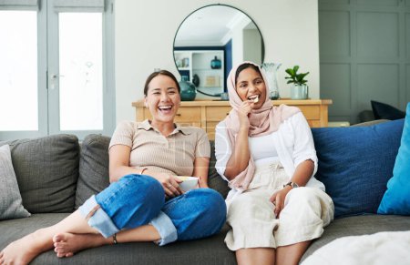 Téléchargez les photos : Femmes amis et manger sur le canapé avec le sourire pour heureux dans la maison pour se détendre avec collation. Les femmes, canapé et salon et rire avec islam pour la diversité avec asiatique avec streaming dans l'appartement. - en image libre de droit