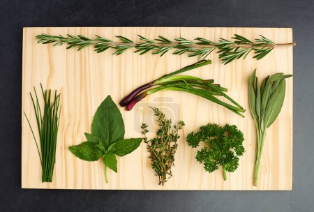 Photo for Basil, thyme, and rosemary on chopping block for nutrition, health and adding flavour to food. Green herbs, parsley and vegetables on kitchen cutting board for cooking, eating and vegan diet. - Royalty Free Image